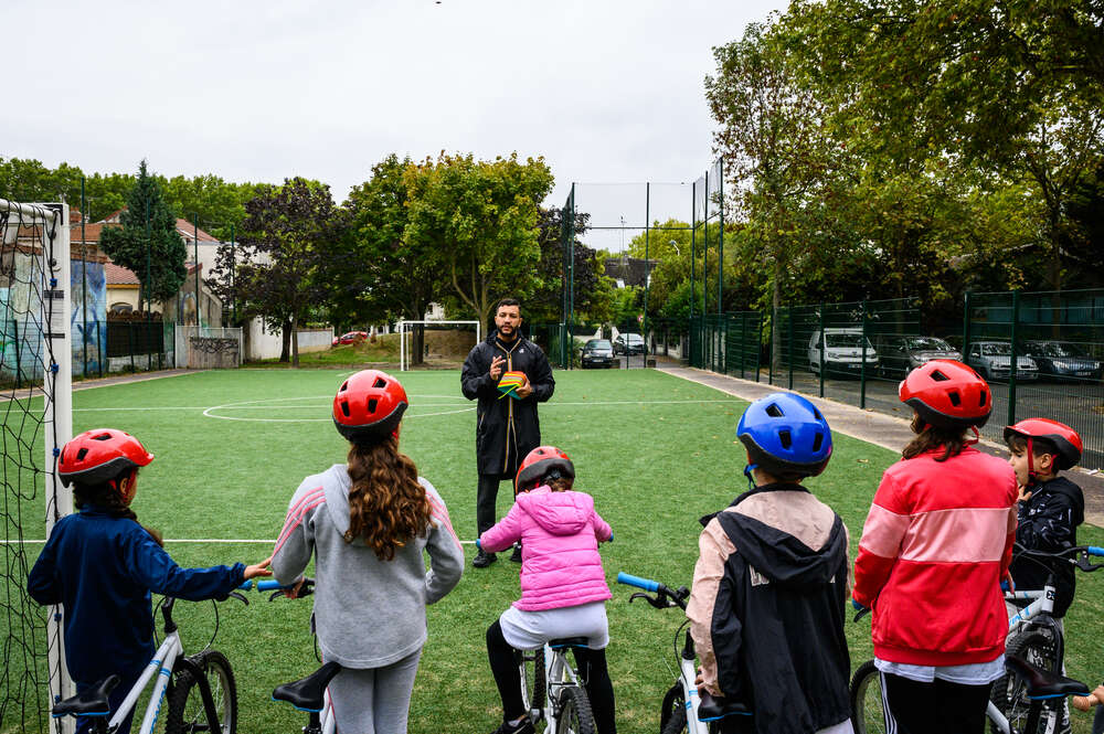 Groupe d'enfants muni de casques et tenant chacun un vélo à la main face à un homme leur donnant des indications